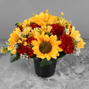 Artificial yellow sunflowers, mini-sunflowers, and red carnations, with gyp and greenery in a full black plastic grave flower pot.