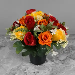 Artificial red rosebud, orange & red open roses, and yellow roses, with gyp and greenery in a black plastic grave flower pot.