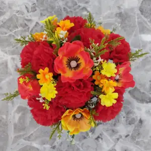 Artificial red/orange and orange/yellow anemones, cream carnations, and yellow & orange cosmos, with gyp and greenery in a full black plastic grave flower pot.